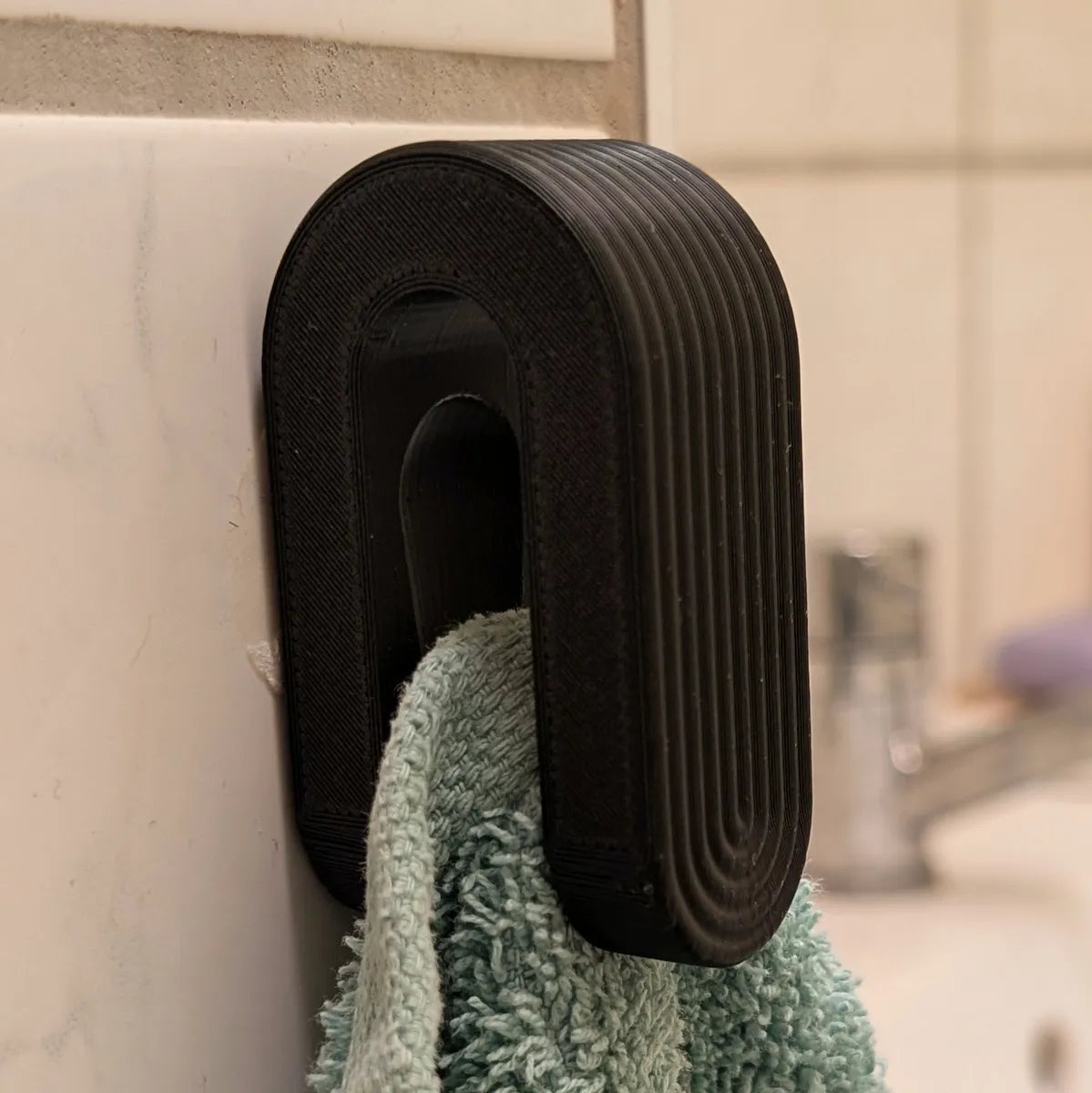 3D printed ball pinch towel hook mounted on wall holding green towel